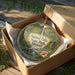 A decorative ornament in a wooden box, featuring a tropical landscape with a waterfall and various flora.