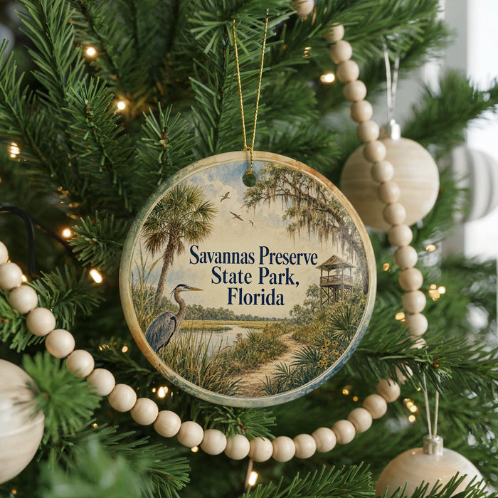 A round ornament hanging on a Christmas tree, featuring a scenic image of a bird and palm trees, with the text "Savannas Preserve State Park, Florida" displayed on it.