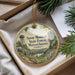 A decorative ornament with a scenic mountain landscape and a lookout tower, placed in a box with pine branches.