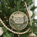 A round ornament hanging on a Christmas tree, featuring a scenic landscape with a tower in the background.