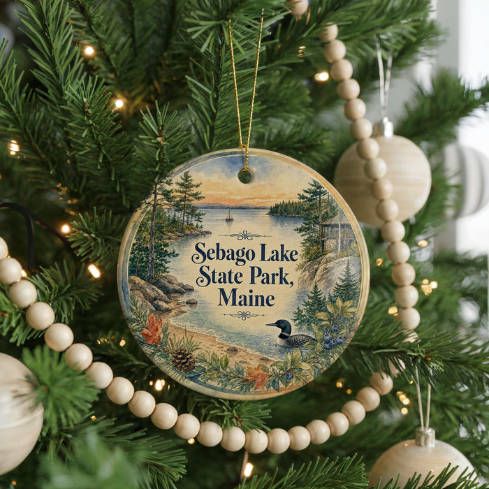 A round ornament hanging on a Christmas tree, featuring a scenic landscape with a lake, pine trees, and a bird.