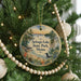 A round ornament hanging on a Christmas tree, featuring a scenic landscape with a lake, pine trees, and a bird.
