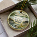 A decorative ornament in a box, featuring a scenic image of Seneca Creek State Park, Maryland.