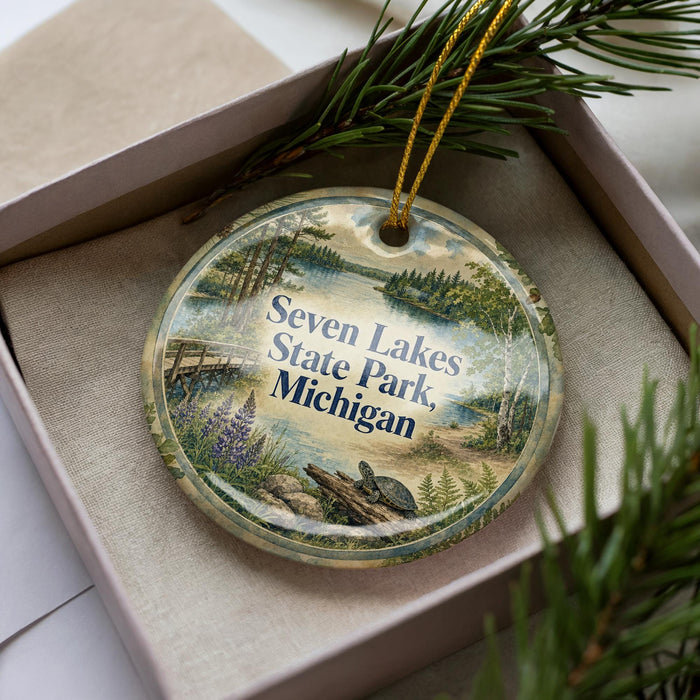 A decorative ornament with a scenic landscape of Seven Lakes State Park, Michigan, displayed in a box with pine branches.