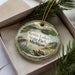 A decorative ornament with a scenic landscape of Seven Lakes State Park, Michigan, displayed in a box with pine branches.