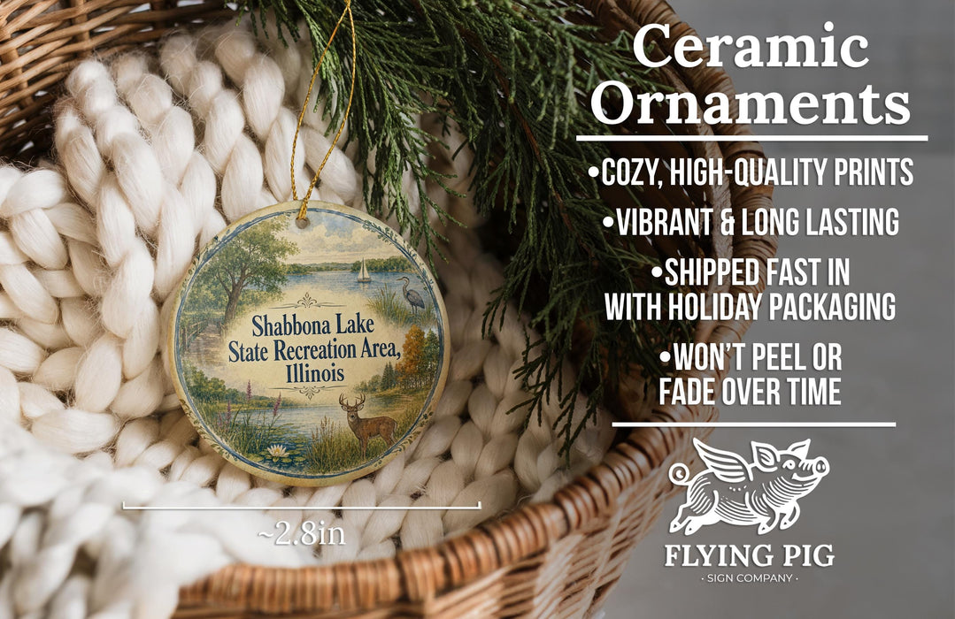 Ceramic ornaments, specifically Shabbona Lake State Recreation Area, Illinois ornaments, are displayed in a basket with greenery. The text highlights the ornaments as "cozy, high-quality prints" and "vibrant & long lasting", with a description of their shipping speed and packaging. The image also includes a logo for "Flying Pig - SIGN COMPANY".