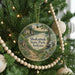 A round ornament hanging on a Christmas tree, featuring a scenic landscape with a house and a lake.