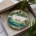 A decorative ornament in a box, featuring an illustration of Silver Springs State Park in Florida with a manatee, palm tree, and other natural elements.