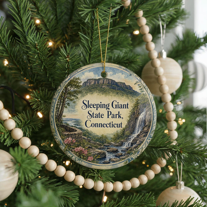 A round ornament hanging on a Christmas tree, featuring a scenic landscape with a waterfall and mountains.