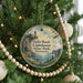 A round ornament hanging on a Christmas tree, featuring a lighthouse and a scenic landscape.
