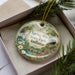 A decorative ornament in a box, featuring a scenic image of Spring Mill State Park, Indiana.