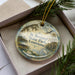 A decorative ornament in a box, featuring a scenic image of St. Bernard State Park in Louisiana.