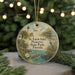 A round ornament with a lighthouse and birds, surrounded by greenery, is displayed in front of a blurred background with twinkling lights.