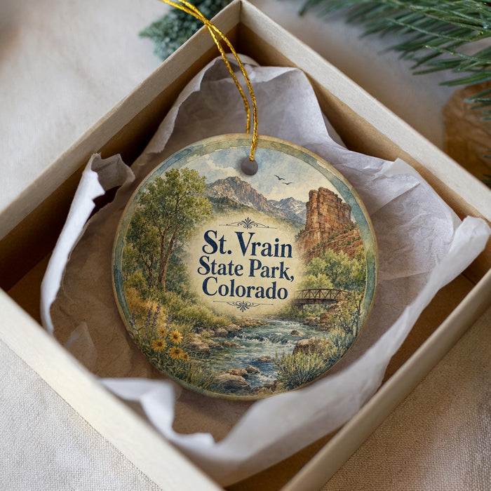 A decorative ornament in a box, featuring a scenic landscape with mountains, trees, and a river.