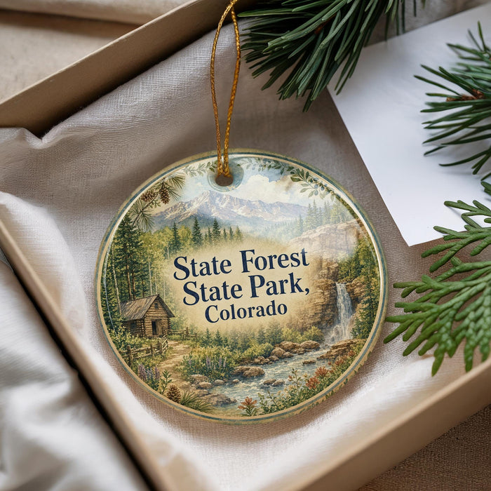 A decorative ornament with a scenic landscape of State Forest State Park, Colorado, featuring a cabin and a waterfall.