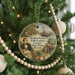 A round ornament hanging on a Christmas tree, featuring an illustration of a man playing a guitar and surrounded by various elements such as a boat, palm trees, and a house.