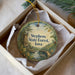 A decorative ornament in a white box, featuring a scenic landscape with a castle, trees, and a river.