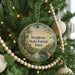 A round ornament hanging on a Christmas tree, featuring a scenic landscape with a castle, trees, and a river.