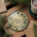 A round ornament with a beach scene and palm trees, featuring the text "Stump Pass Beach State Park, Florida" on it, is displayed on a wooden surface alongside a cup of coffee and some pine branches.