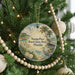 A round ornament hanging on a Christmas tree, featuring a beach scene with palm trees, a bird, and a body of water.
