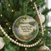 A round ornament hanging on a Christmas tree, featuring a scenic landscape with a lake, trees, and a deer.