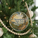 A round ornament hanging on a Christmas tree, featuring a scenic landscape with a river and mountains.
