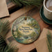 A decorative ornament featuring a scenic view of Suwannee River State Park in Florida, with a bird, flowers, and a boat on the water.
