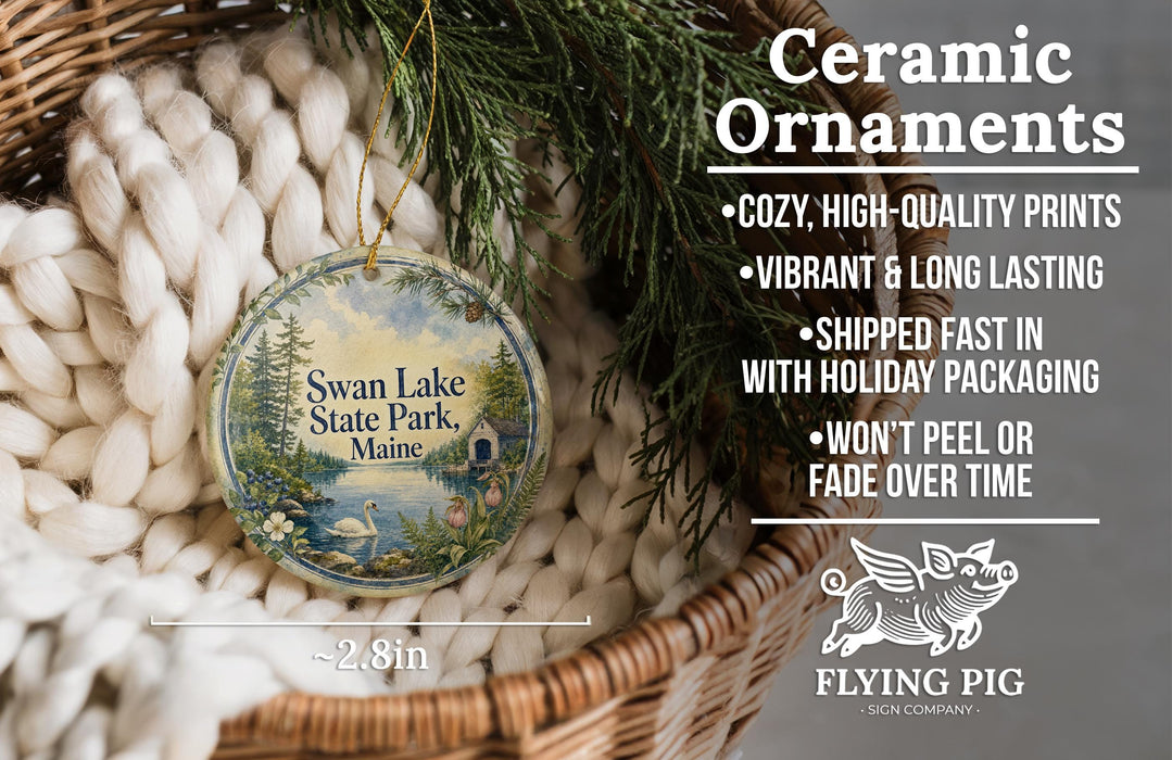 Ceramic ornaments, featuring a design of Swan Lake State Park, Maine, with a wicker basket and greenery in the background.