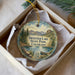 A decorative ornament in a box, featuring a scenic landscape with mountains, trees, and a lake.