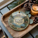 A wooden tray with a decorative ornament featuring a scenic landscape of Sylvan Lake State Park, Colorado, and pine cones.