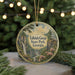 A circular ornament with a scenic landscape of Tallulah Gorge State Park, Georgia, featuring a waterfall and pine trees, is displayed on a table with Christmas lights in the background.