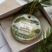 A decorative ornament with a scenic image of Taylorville Lake, State Park, and Kentucky, featuring a bird, flowers, and a castle, is displayed in a box with pine branches.