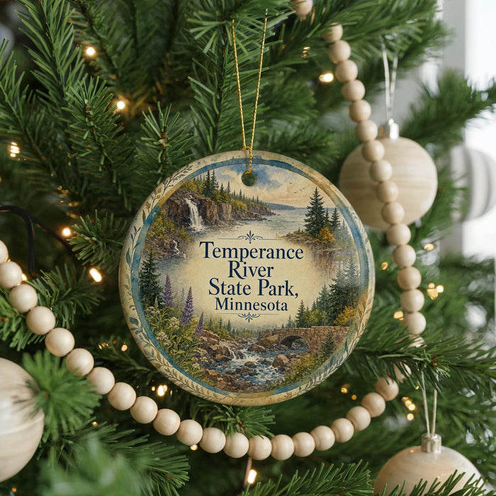 A circular ornament hanging on a Christmas tree, featuring a scenic landscape with a waterfall and pine trees.