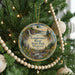 A circular ornament hanging on a Christmas tree, featuring a scenic landscape with a waterfall and pine trees.