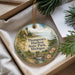 A decorative ornament with a lighthouse and a scenic landscape, placed in a box with pine branches.