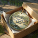 A decorative ornament in a wooden box, featuring a scenic image of the Tippecanoe River State Park in Indiana.