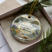 A decorative ornament with a scenic image of Tomales Bay State Park, California, displayed in a box with pine branches.