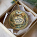 A decorative ornament in a box, featuring a scenic landscape with a bridge, cactus, and water.