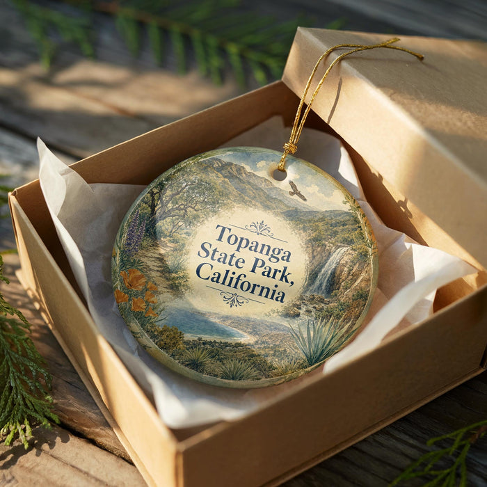 An oval ornament in a brown box, featuring a scenic landscape with mountains, trees, and a waterfall.