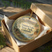 A decorative ornament in a box, featuring a scenic landscape with mountains and a lake, with the text "Trinidad Lake State Park, Colorado" printed on it.