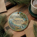 A decorative ornament featuring a scenic image of Turlock Lake, with a boat and a bird in the foreground, surrounded by pine branches and a cup of coffee on a wooden surface.