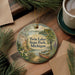 A decorative ornament featuring a scenic lake landscape with a canoe, surrounded by pine trees and a wooden dock, placed on a wooden surface alongside a cup of coffee and some papers.
