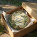 A decorative ornament in a wooden box, featuring a scenic landscape with a lake, pine trees, and a boat, with the text "Twin Lakes State Park, Michigan" displayed on the ornament.