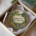 A decorative ornament in a box, featuring a scenic landscape with a river, trees, and a castle.