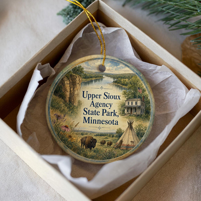 A decorative ornament in a box, featuring a scenic landscape with a house, a cow, and a teepee, along with the text "Upper Sioux Agency State Park, Minnesota".