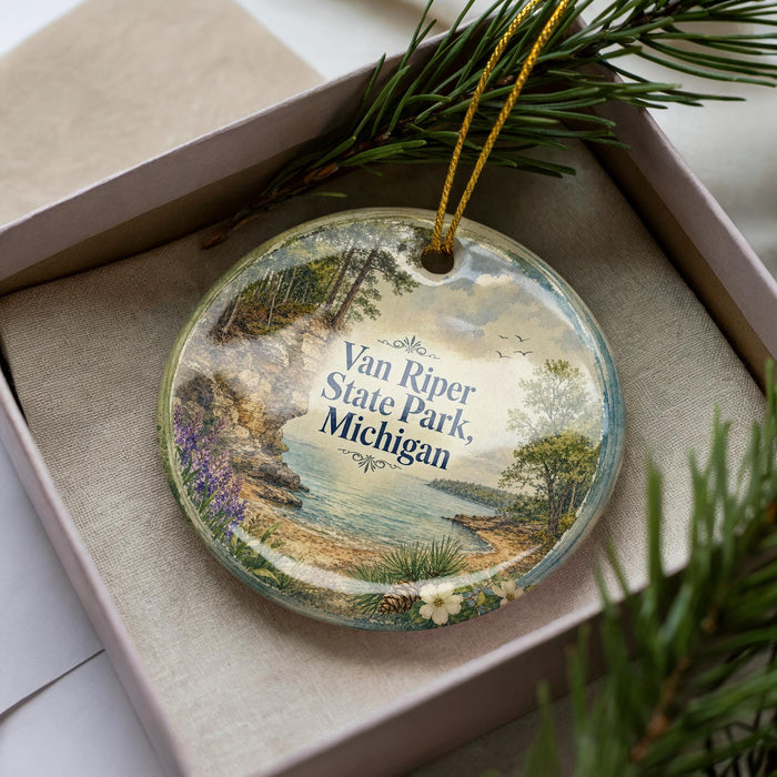 A decorative ornament with a scenic landscape of Van Riper State Park, Michigan, displayed in a box with pine branches.