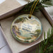 A decorative ornament with a scenic landscape of Van Riper State Park, Michigan, displayed in a box with pine branches.