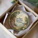 A decorative ornament in a box, featuring a scenic landscape with a lake, mountains, and trees.