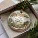 A decorative ornament in a box, featuring a scenic landscape with mountains, trees, and a sign that says "Vega State Park, Colorado".
