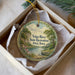 A decorative ornament in a white box, featuring a scenic landscape with a river, trees, and a boat.